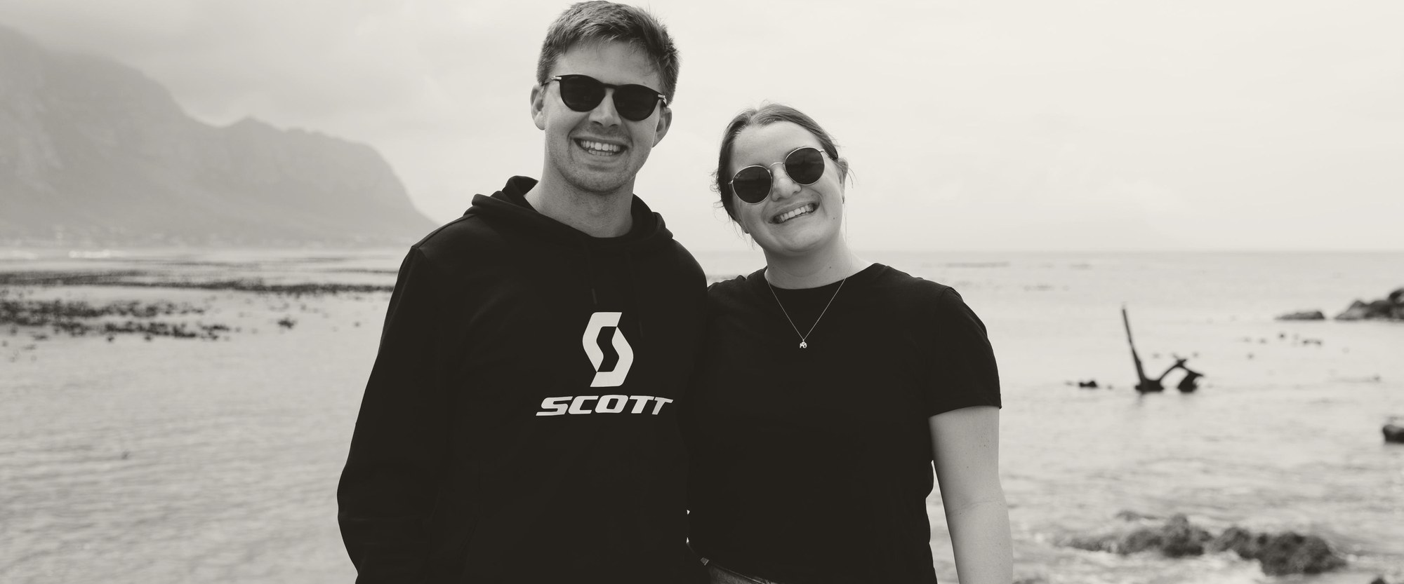 Jacques and Lara by the sea, with the mountains behind, in black and white.